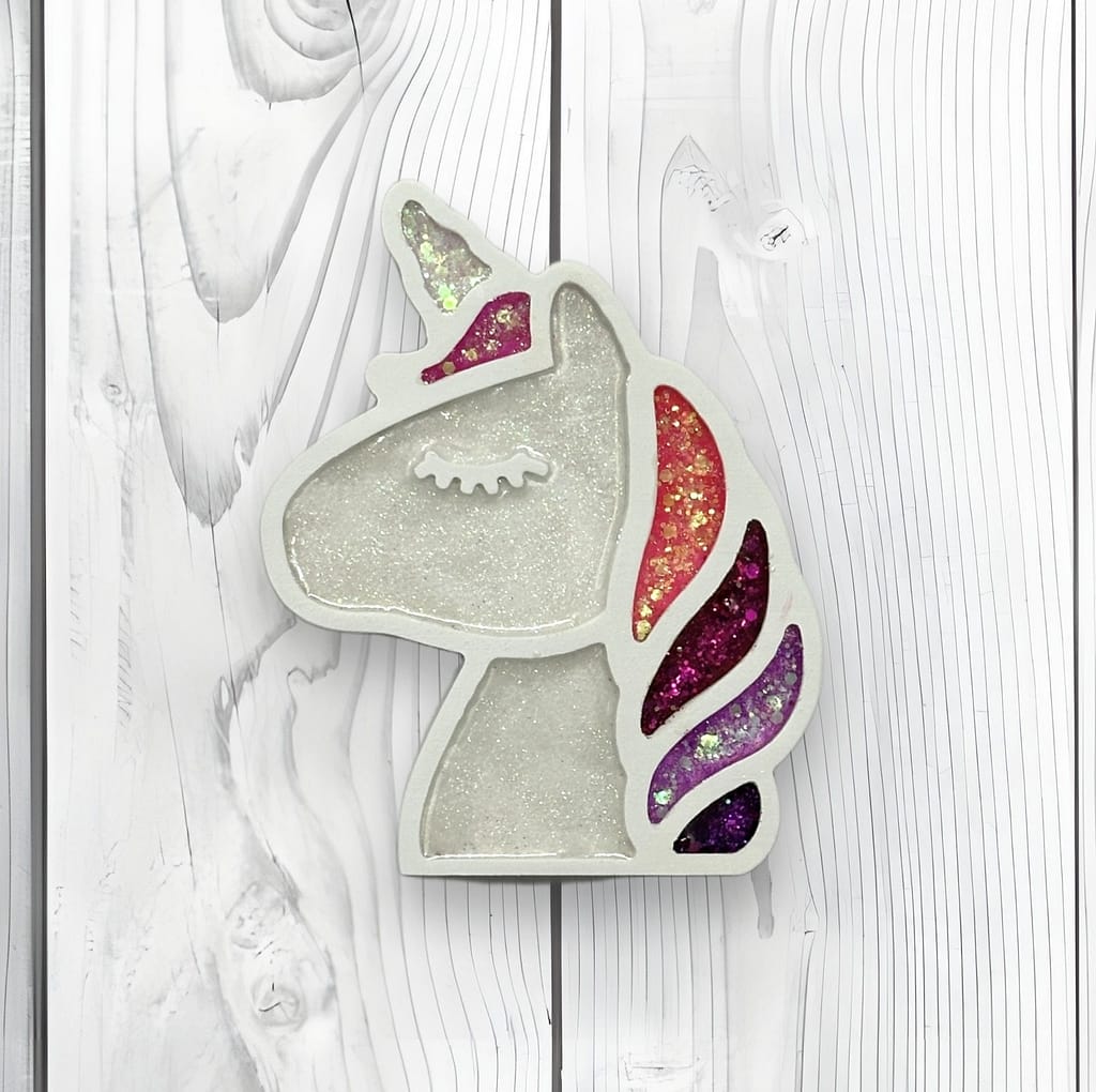 Handmade glitter unicorn wall decor displayed on the wall with simple wood accents.