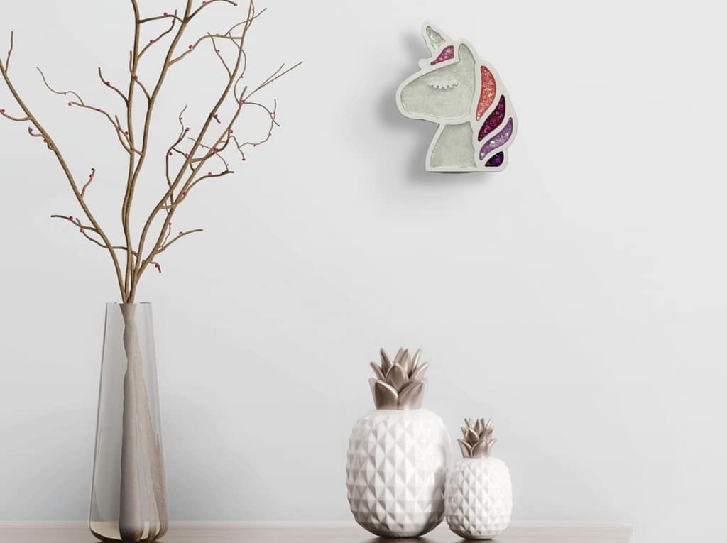 Small glitter unicorn wall art displayed on a modern white wall above decorative vases and branches.