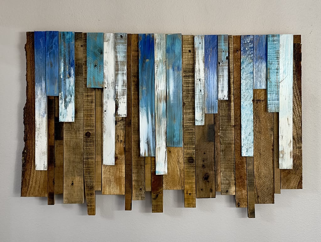 Large reclaimed wood wall art with blue, white, and natural brown vertical planks hanging on a light wall