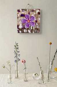 Close-up of a purple metal flower wall art piece mounted on distressed wood with white and plum tones