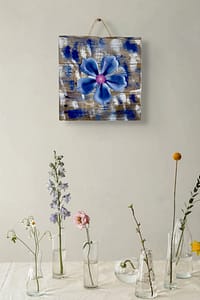 Close-up of a blue metal flower wall art piece mounted on distressed wood with white and blue paint