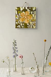 Close-up of a yellow metal flower wall art piece mounted on distressed wood with warm neutral tones