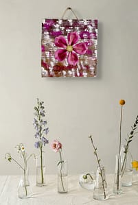 Close-up of a pink metal flower wall art piece mounted on distressed wood with white and magenta paint