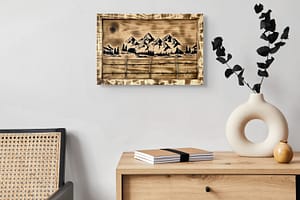 Frontier Springline Mountain Fence wood wall art hanging above a wooden cabinet with books and a vase