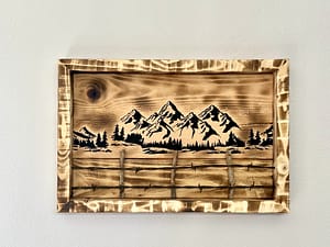 Close-up of a wood burned mountain and fence scene with trees and rustic burned wood grain