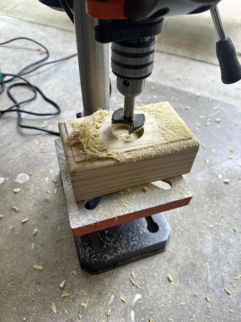 Drill press carving tealight holes in wooden block.
