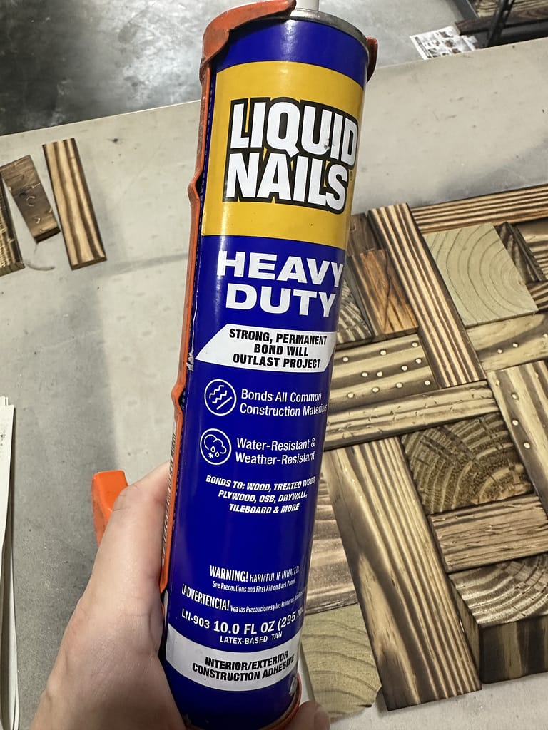 Liquid Nails heavy-duty glue held in front of Shou Sugi Ban geometric mosaic wood pieces before assembly.