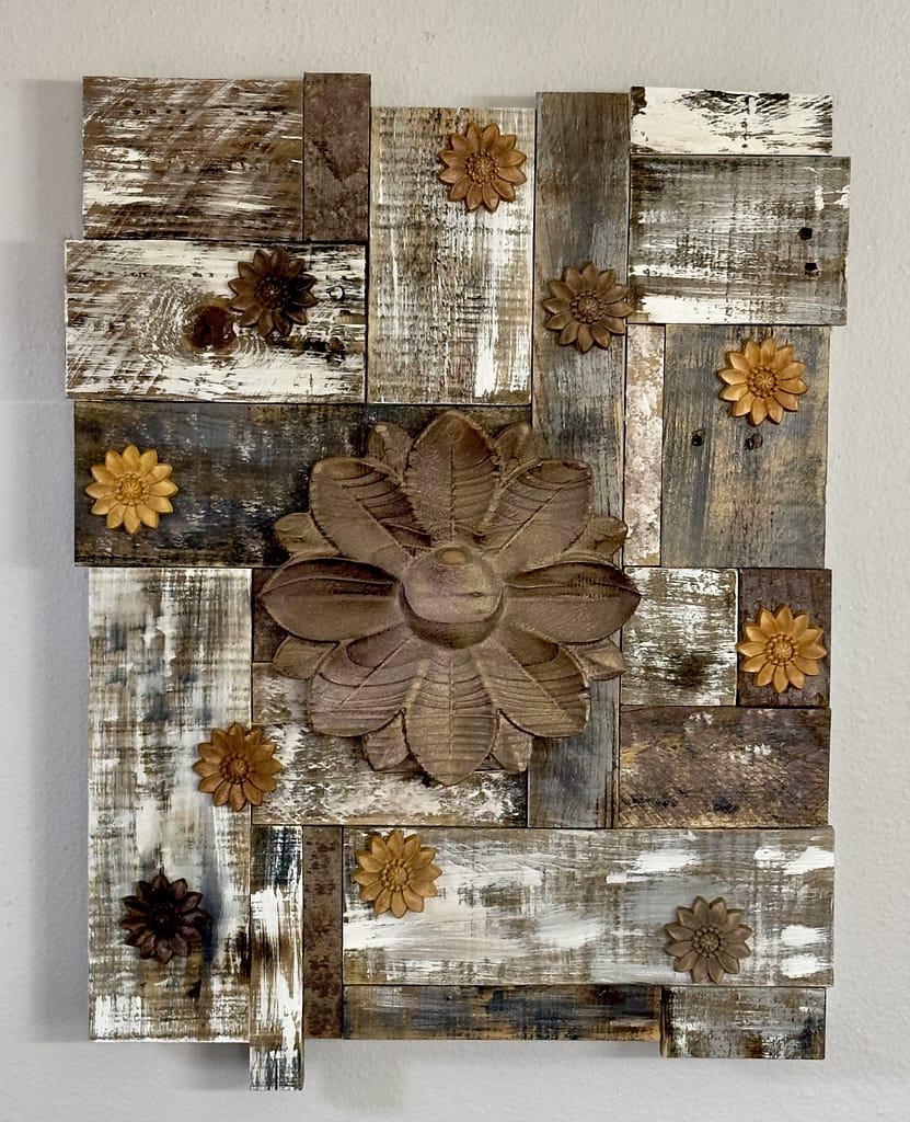Rustic reclaimed wood wall art with carved central flower and small flowers on a distressed white and brown wood background